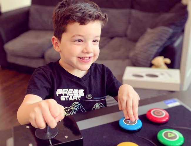 wilson_1000 Smiling young boy pressing a button on an adapted gaming setup