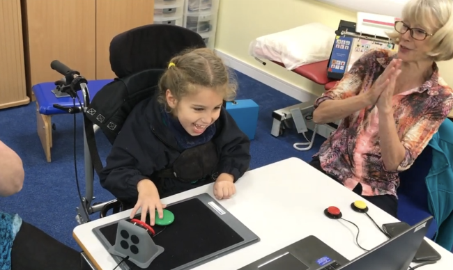 Young girl laughs as she presses a switch to operate a computer