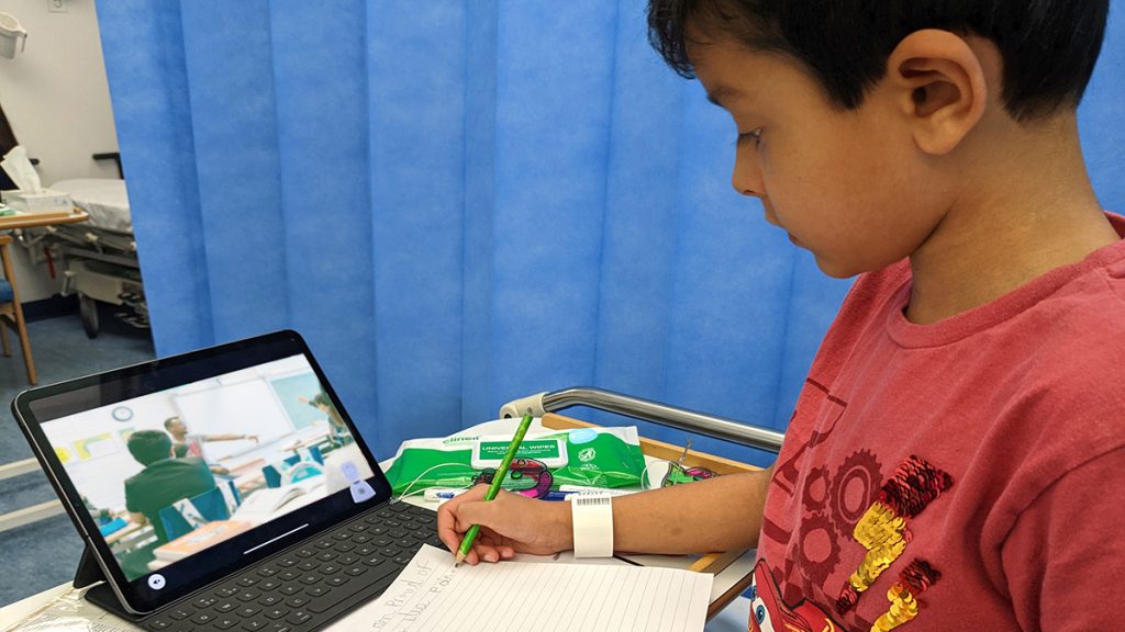 Young boy in hospital looking at an iPad screen showing a classroom