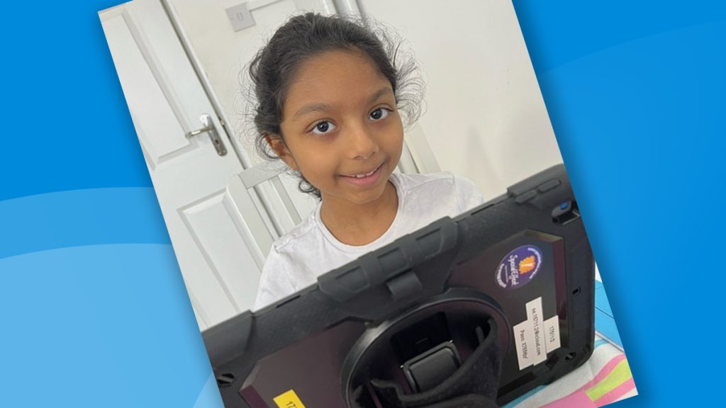 Young girl smiling at the camera from behind a tablet computer